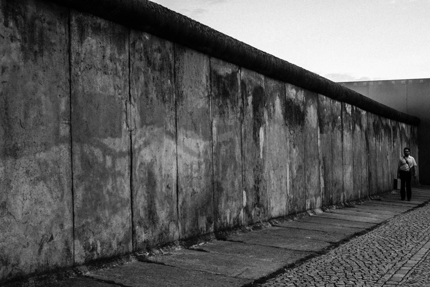 Bernauer Stra&szlig;e — a film crew restages a man with a briefcase walking the cobbled patrol road inside the preserved death-strip apparatus.