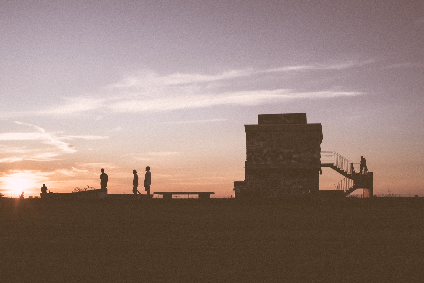 A handful of skater silhouettes at the edge of the Tempelhof apron at sunset; the abandoned terminal a dark mass against the orange sky.