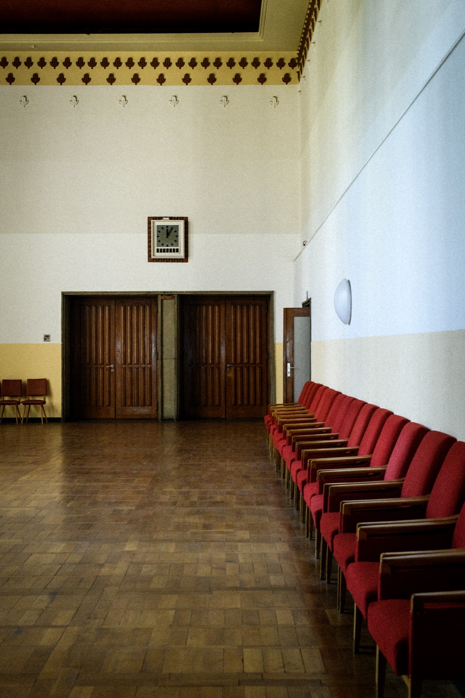 A formal interior at Funkhaus &mdash; a row of red velvet chairs, a clock above them, a closed double door, parquet floor.