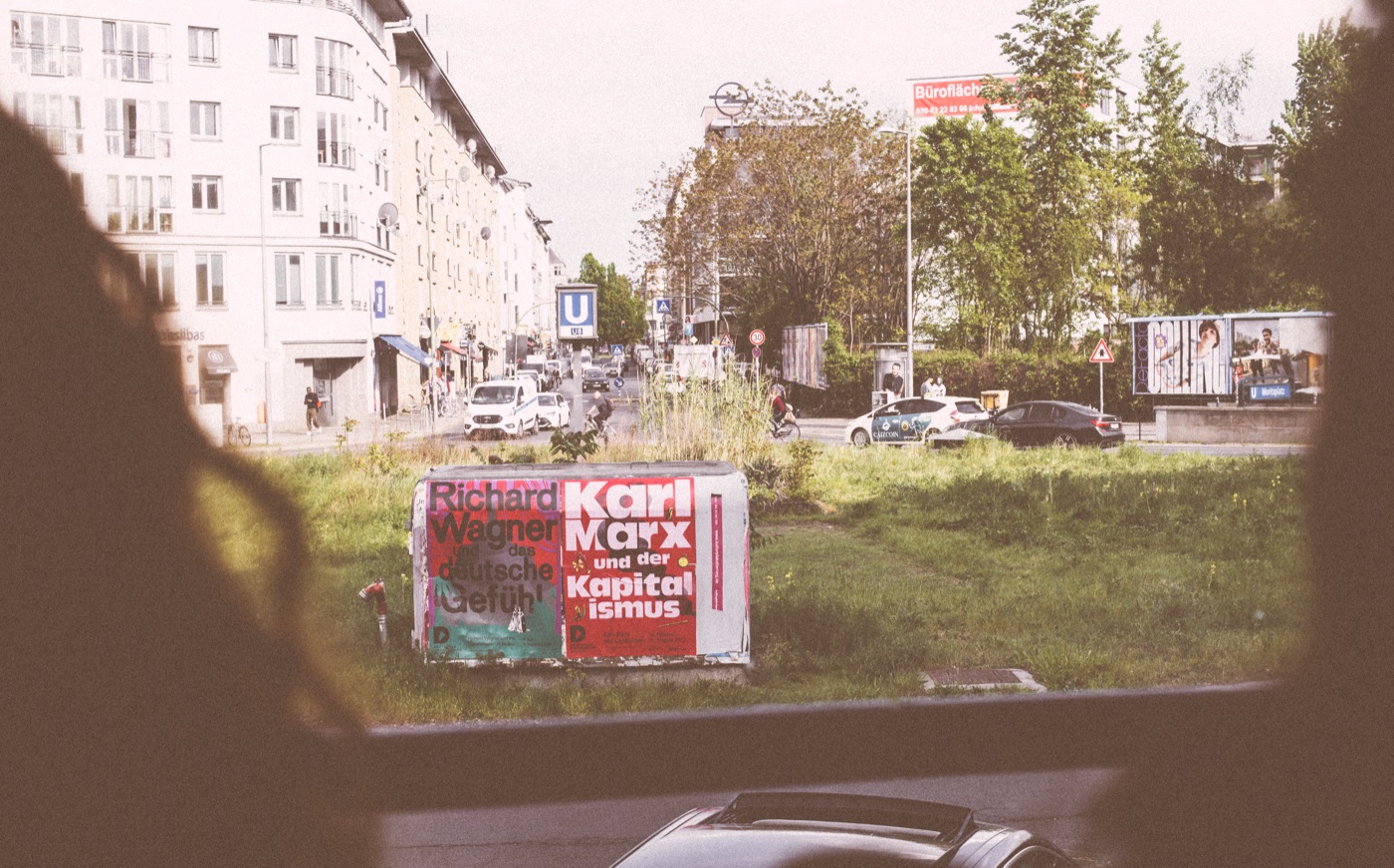 A bus moves through the Moritzplatz traffic circle; Berlin lecture-series posters on the traffic-circle island.