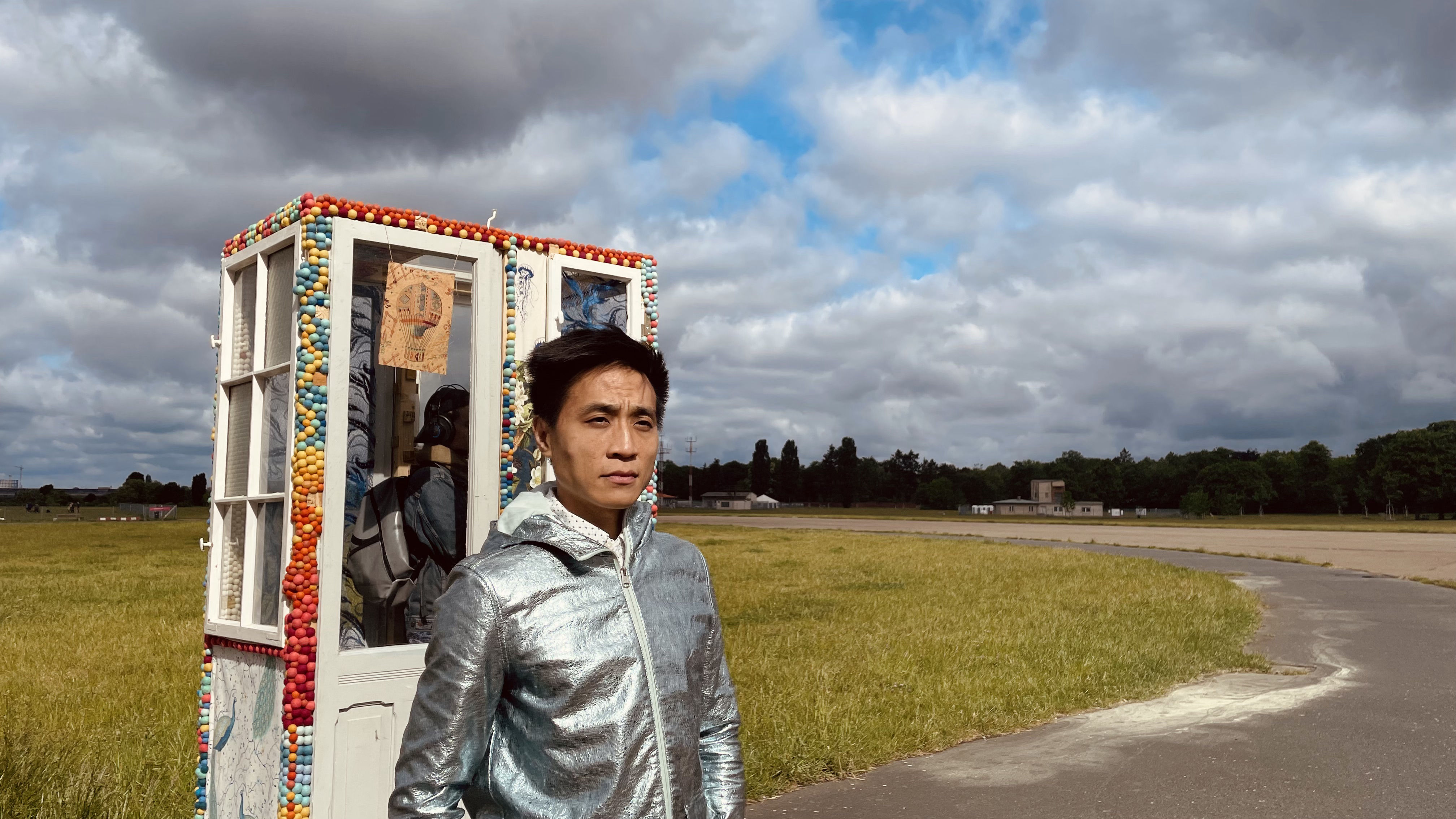 Photo of Eric Pan standing at his teleporter / phone-booth art installation, Tempelhoferfeld, Berlin